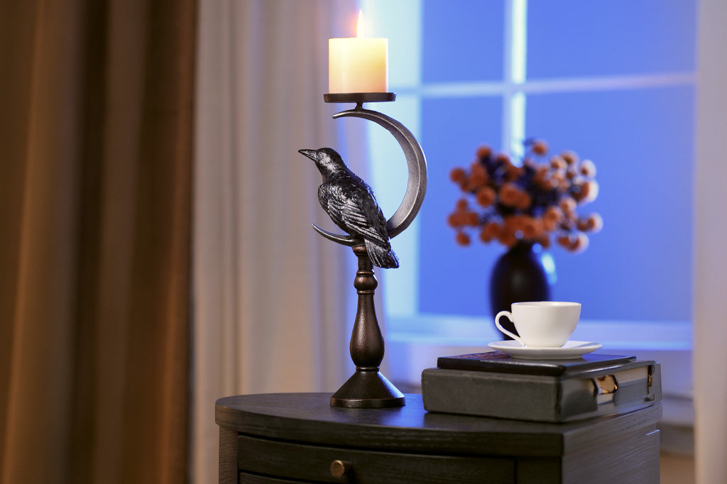 Decorative candle holder with a bird design on a nightstand next to a cup and books.