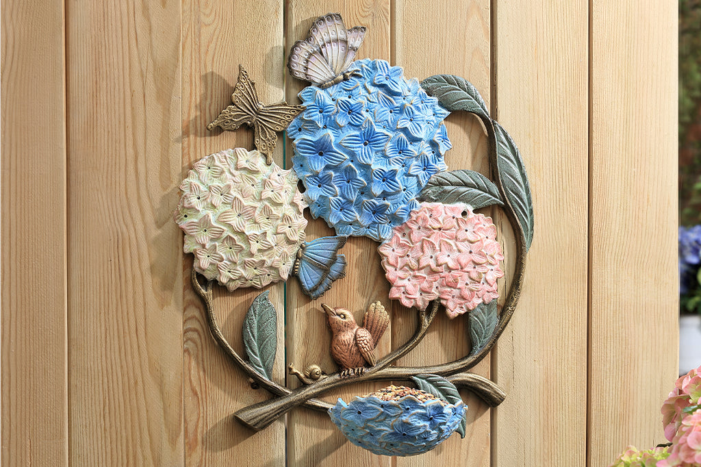 A round, wall mounted bird feeder with details of hydrangeas, leaves, birds, butterflies, and snails.