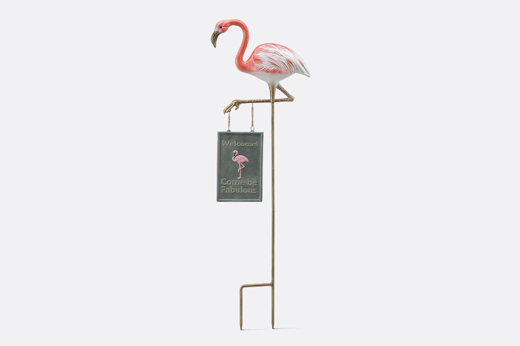 A staked garden sign of a flamingo that says "Welcome! Come be fabulous."