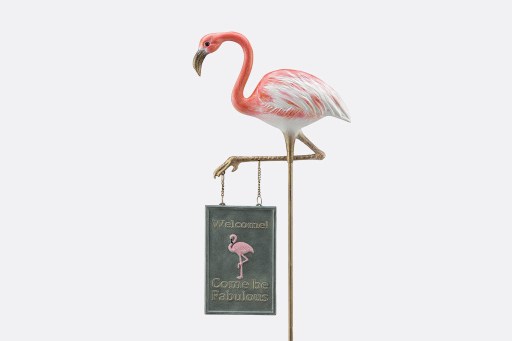 A staked garden sign of a flamingo that says "Welcome! Come be fabulous."