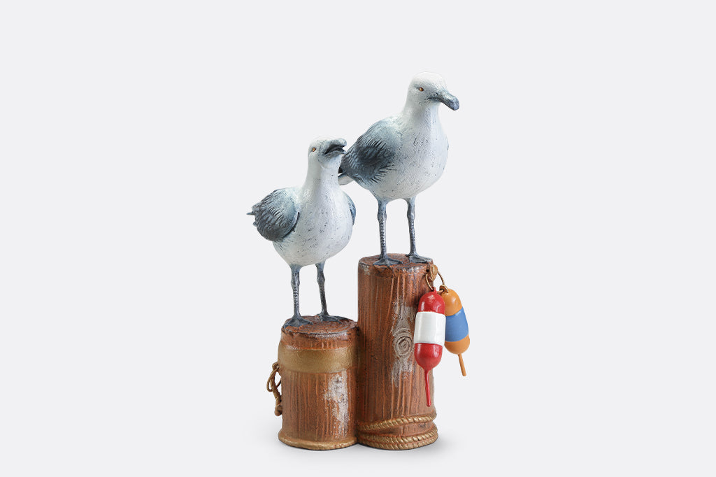 A sculpture of two seagulls standing atop the supporting beams of a dock adorned in buoys and rope.