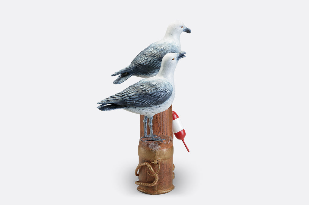 A sculpture of two seagulls standing atop the supporting beams of a dock adorned in buoys and rope.