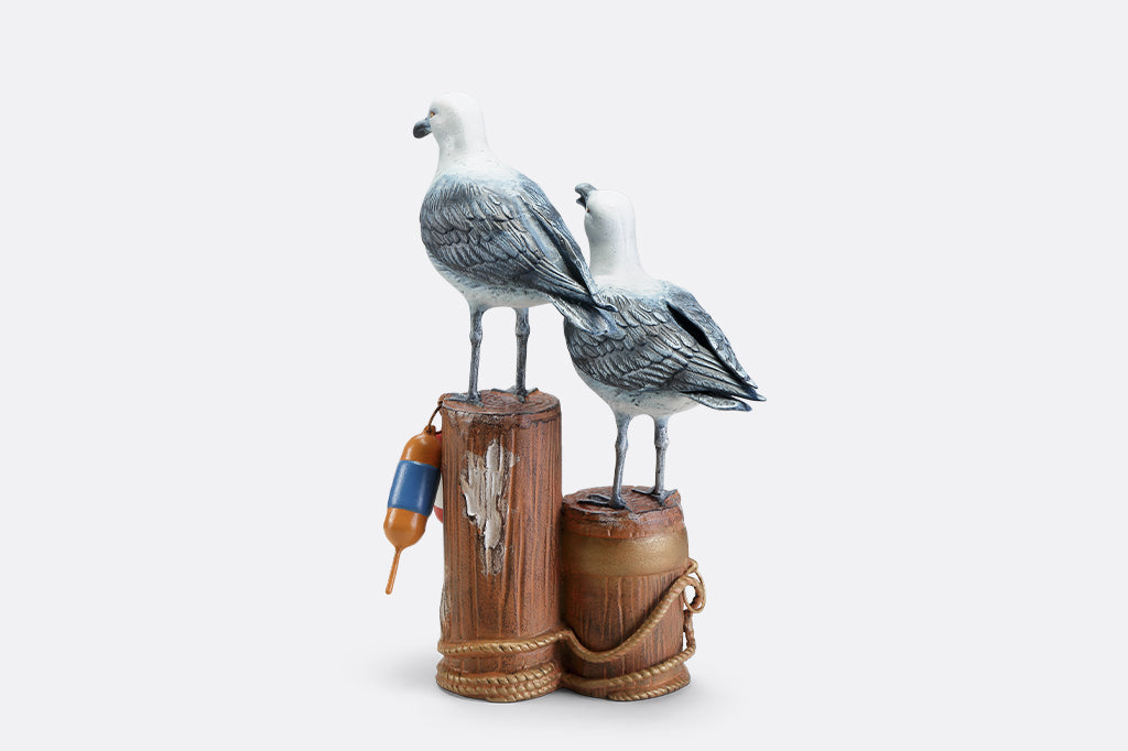 A sculpture of two seagulls standing atop the supporting beams of a dock adorned in buoys and rope.
