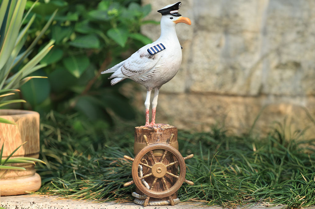 A sculpture of a seagull dressed in Captain regalia standing atop a dock adorned with rope and a ship's steering wheel.