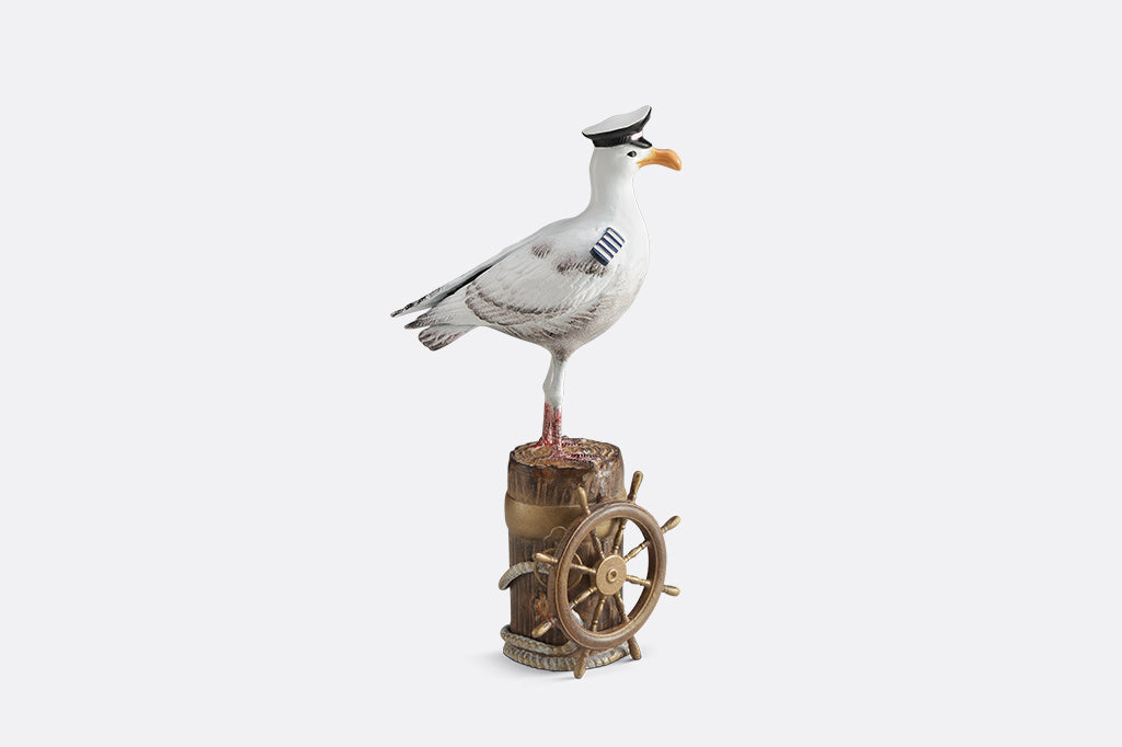 A sculpture of a seagull dressed in Captain regalia standing atop a dock adorned with rope and a ship's steering wheel.
