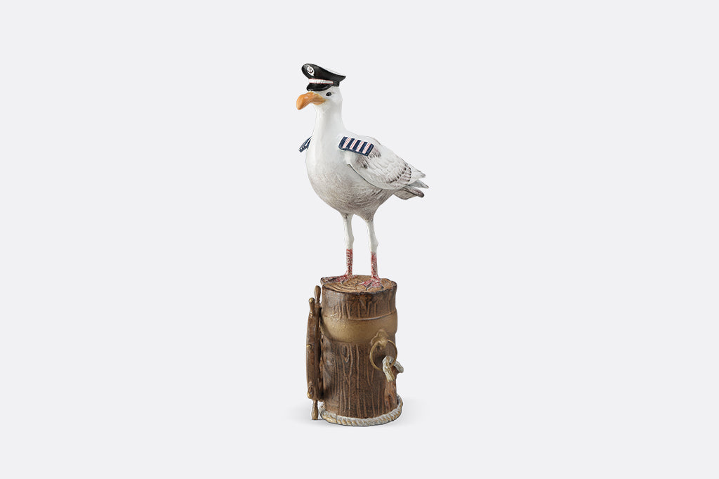 A sculpture of a seagull dressed in Captain regalia standing atop a dock adorned with rope and a ship's steering wheel.