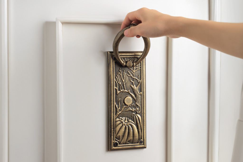 Decorative brass door knocker on a white door with a hand reaching to press it.