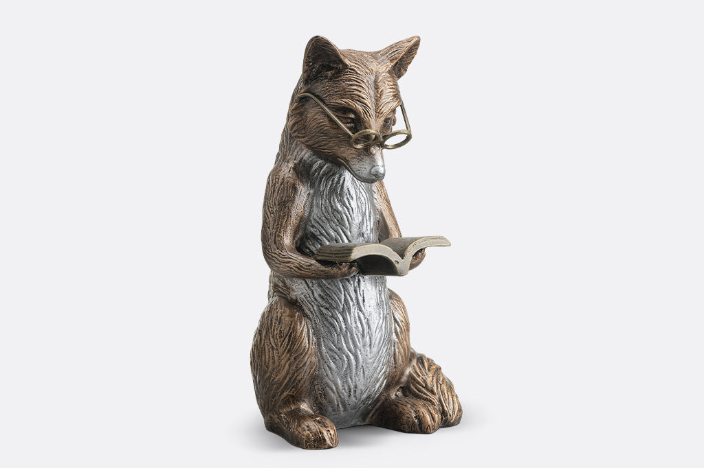 Statue of a fox wearing glasses and reading a book on a white background