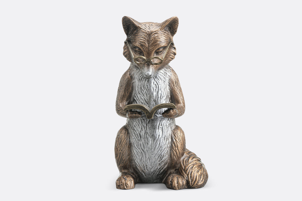 Statue of a fox sitting and reading a book on a white background