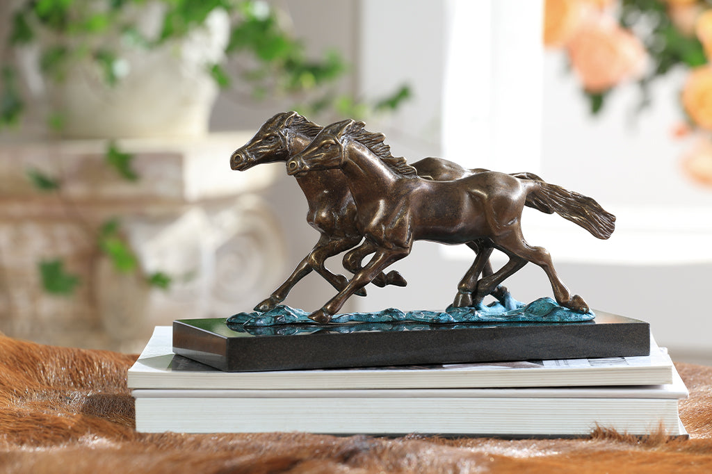 Brass sculpture of two horses running on water on a marble base.