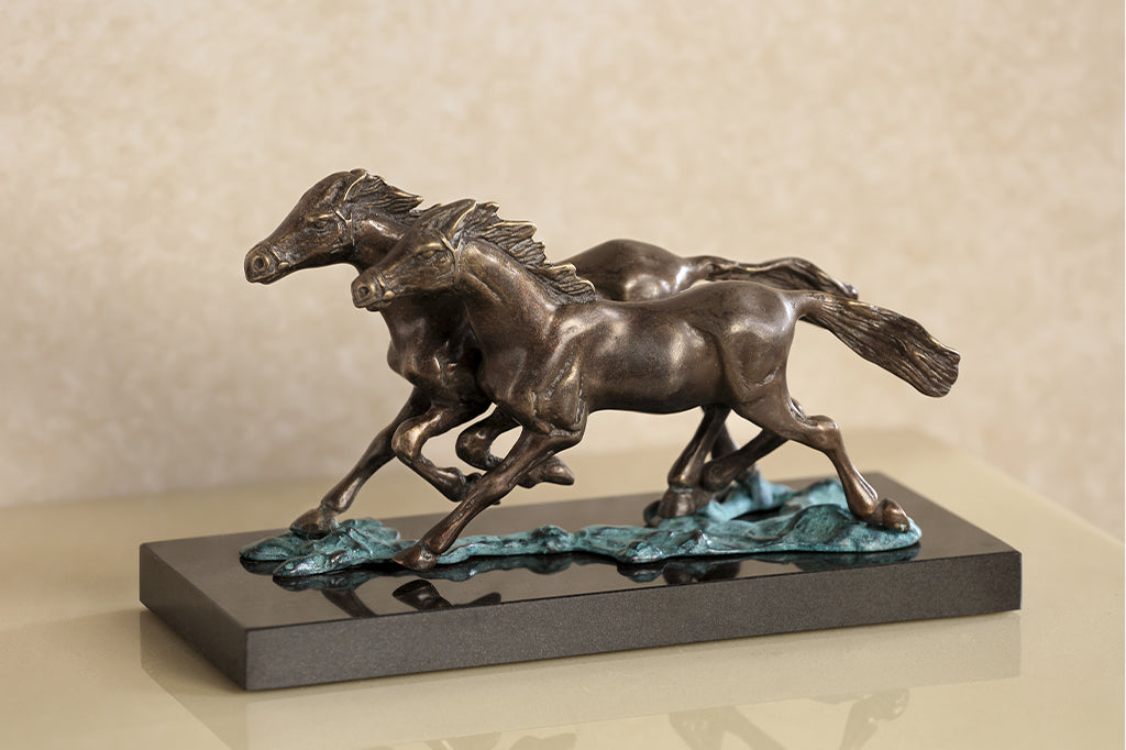 Brass sculpture of two horses running on water on a marble base.