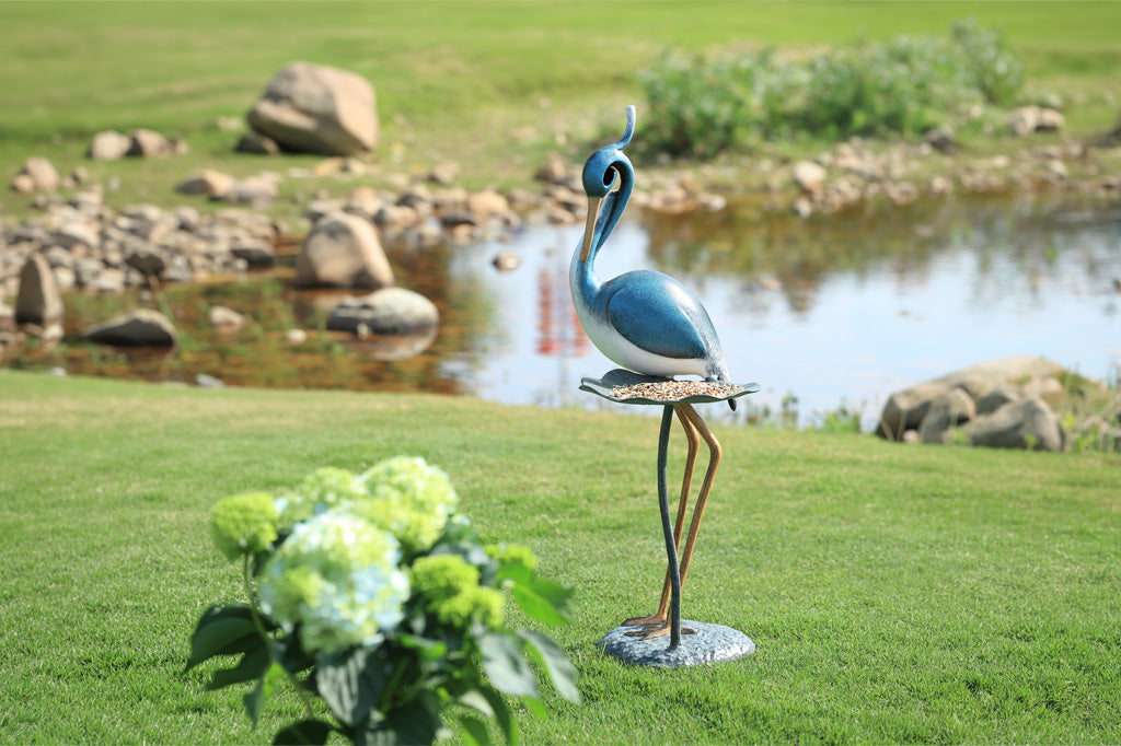 Decorative heron statue on a grassy area with a pond and rocks in the background