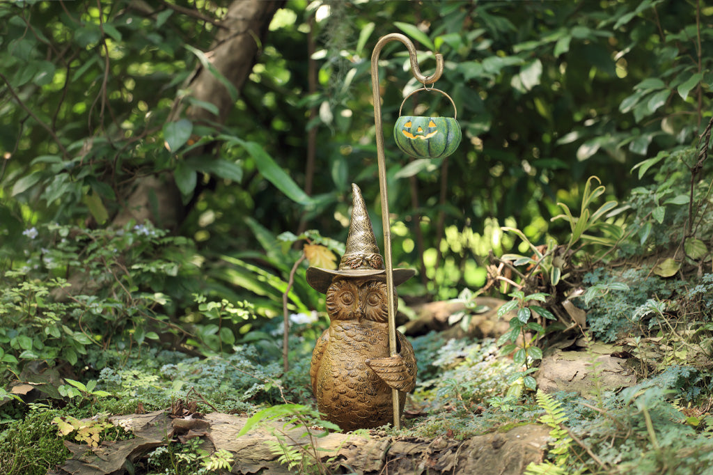 Decorative figure of a creature wearing a pointed hat with a small pumpkin lantern in a forest setting