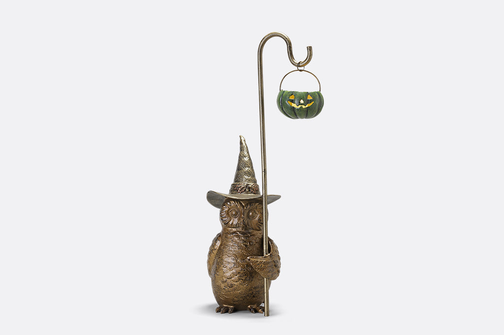 Decorative figure of a creature wearing a pointed hat with a small pumpkin lantern on a white background
