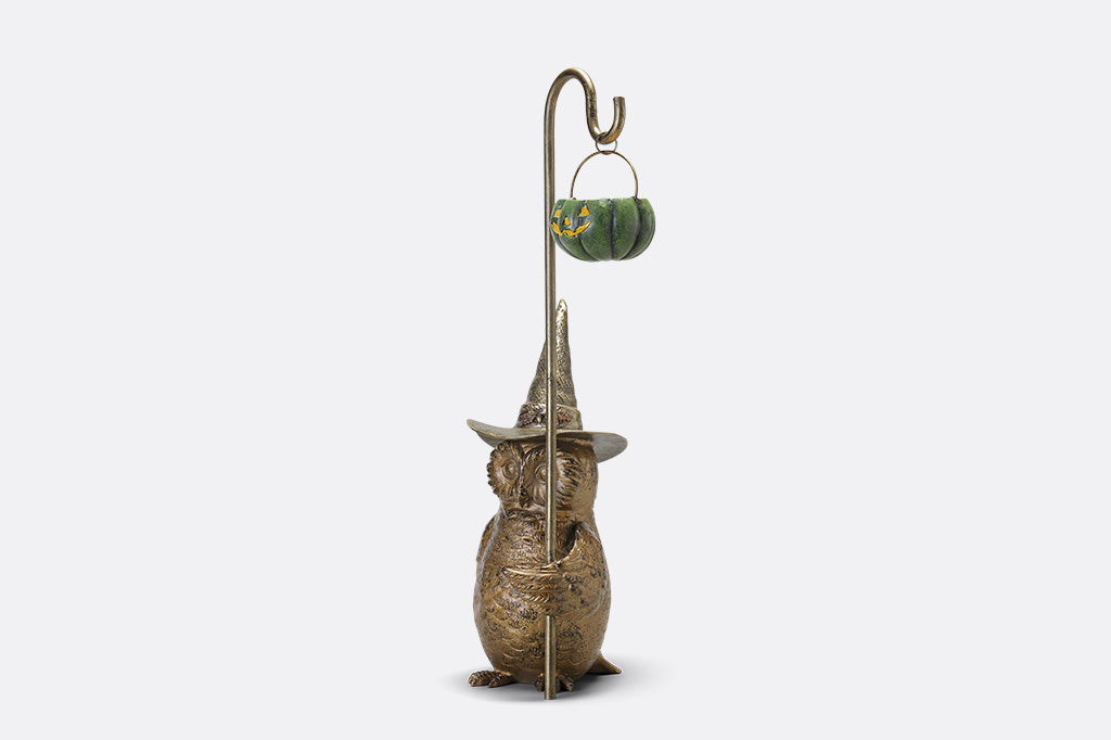 Decorative figure of a creature wearing a pointed hat with a small pumpkin lantern on a white background