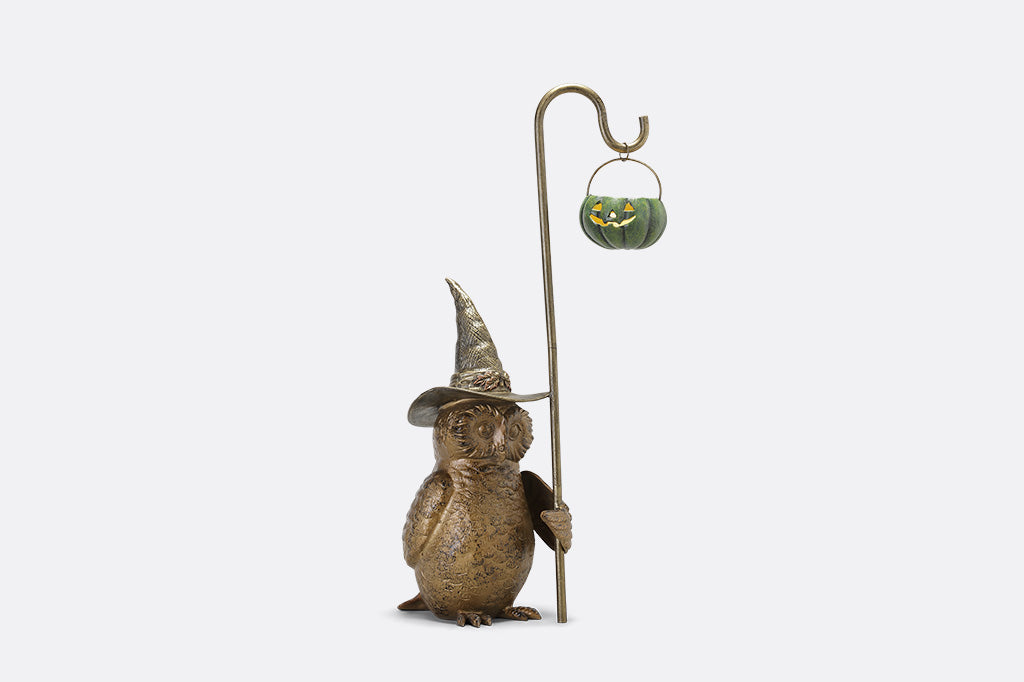 Decorative figure of a creature wearing a pointed hat with a small pumpkin lantern on a white background