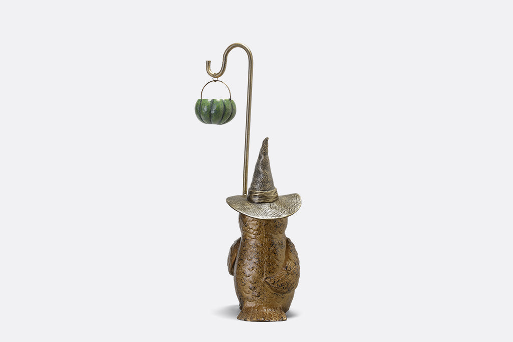 Decorative figure of a creature wearing a pointed hat with a small pumpkin lantern on a white background