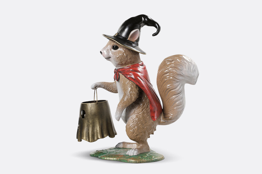 Squirrel figurine wearing a witch hat and holding a bell on a white background