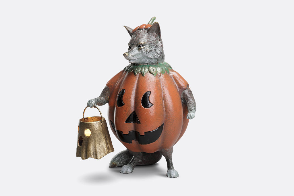 Figurine of a fox in a pumpkin costume holding a lantern on a white background
