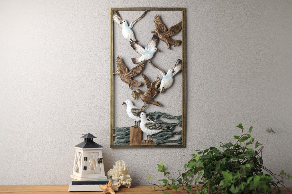 Decorative wall art of birds and a seashell on a gray wall with a small plant and lantern in the foreground.