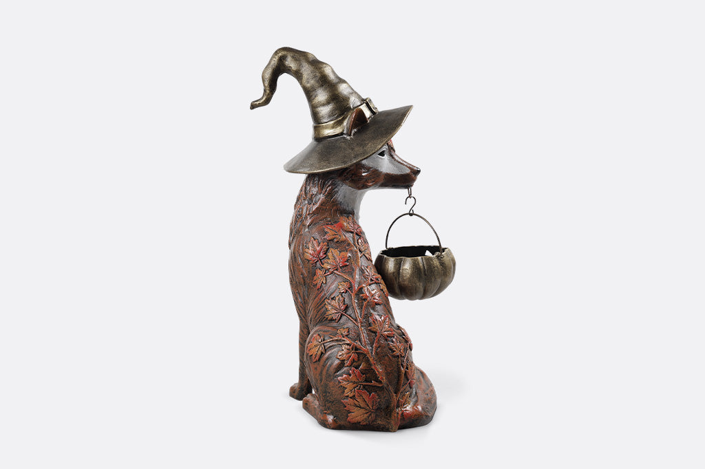 Decorative statue of a dog wearing a witch hat with a small cauldron on a white background