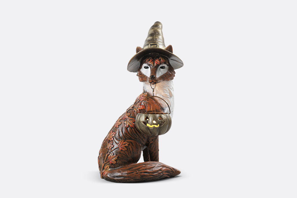 Fox figurine wearing a witch hat with a pumpkin on a white background