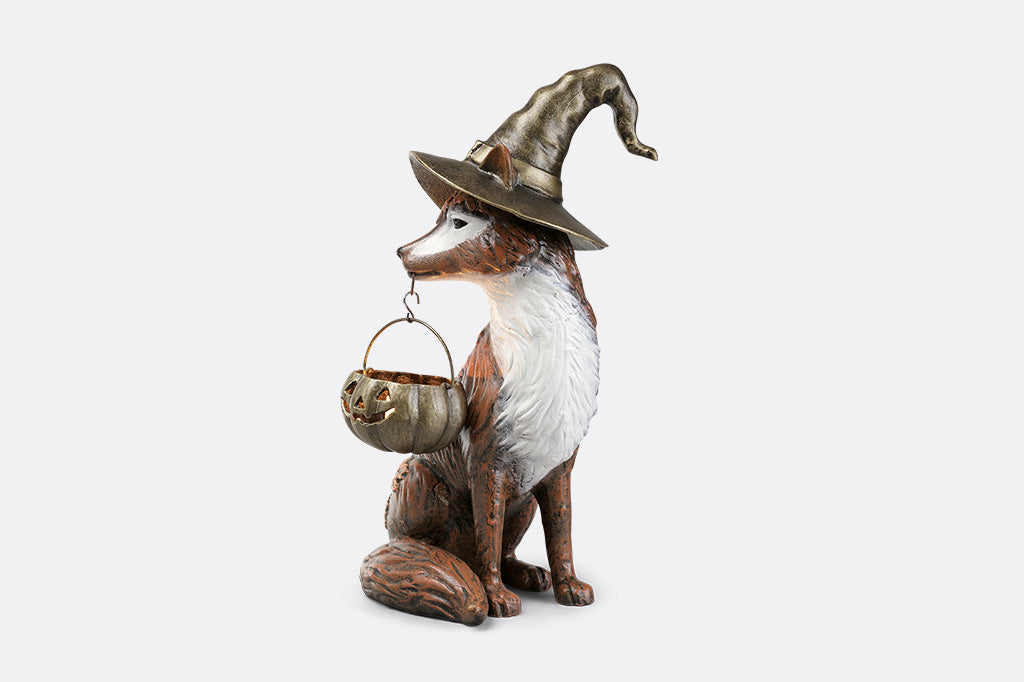 Fox figurine wearing a witch hat with a basket on a white background