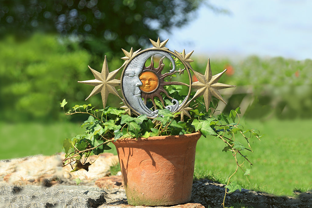 A garden edging with 5 stars, a moon, and a sun inside a potted plant in a garden.
