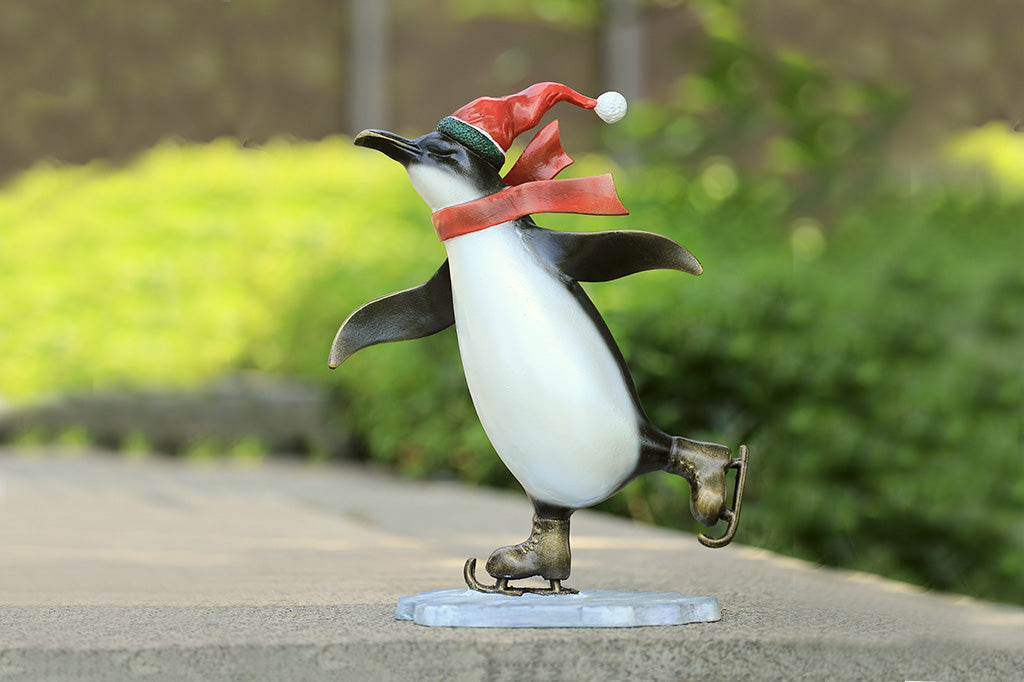 A sculpture of a penguin wearing a scarf and Santa hat ice skating.