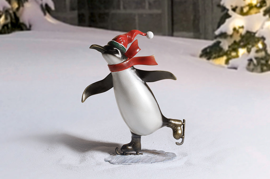 A sculpture of a penguin wearing a scarf and Santa hat ice skating.