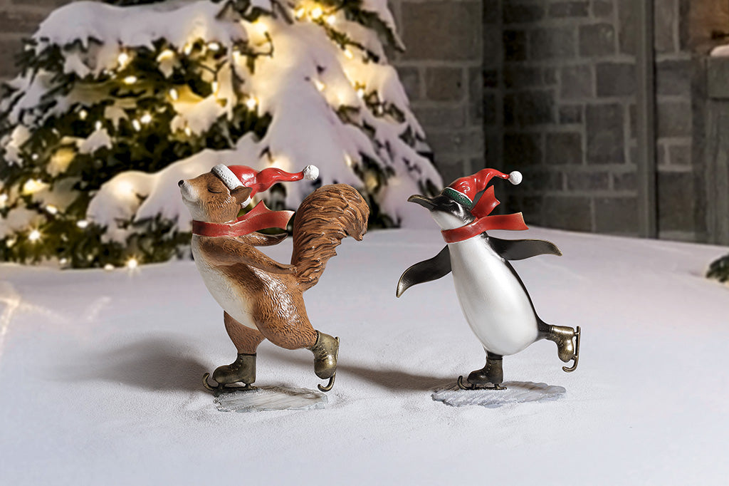 A sculpture of a penguin and a squirrel wearing a scarf and Santa hat ice skating.
