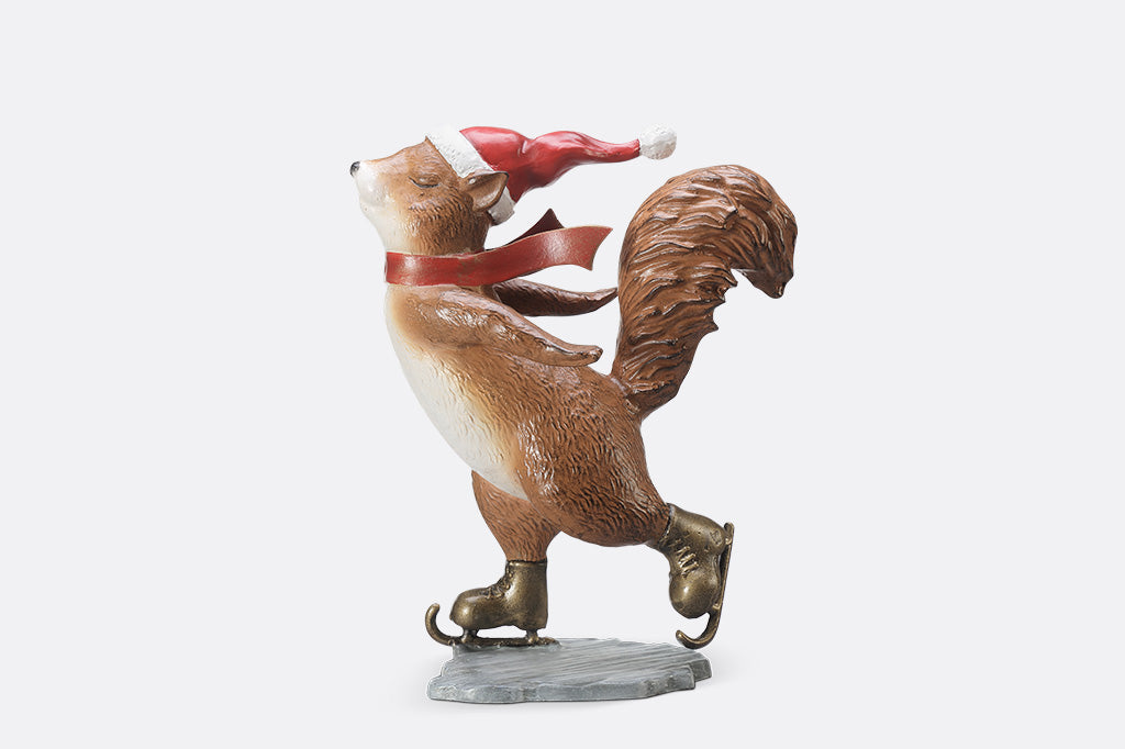 A statue of a squirrel wearing a santa hat and scarf ice skating.