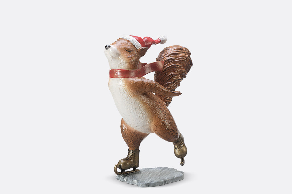 A statue of a squirrel wearing a santa hat and scarf ice skating.