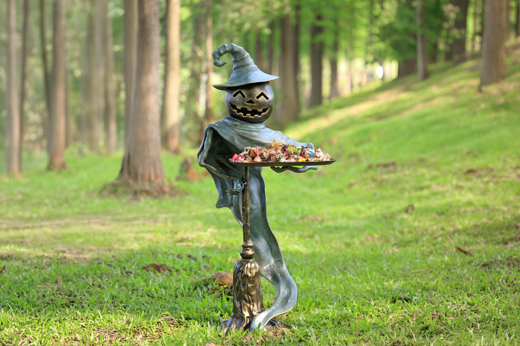 Scarecrow with a pumpkin head holding a tray of candies in a forest setting
