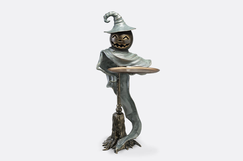 Bronze sculpture of a witch with a broom and hat on a white background