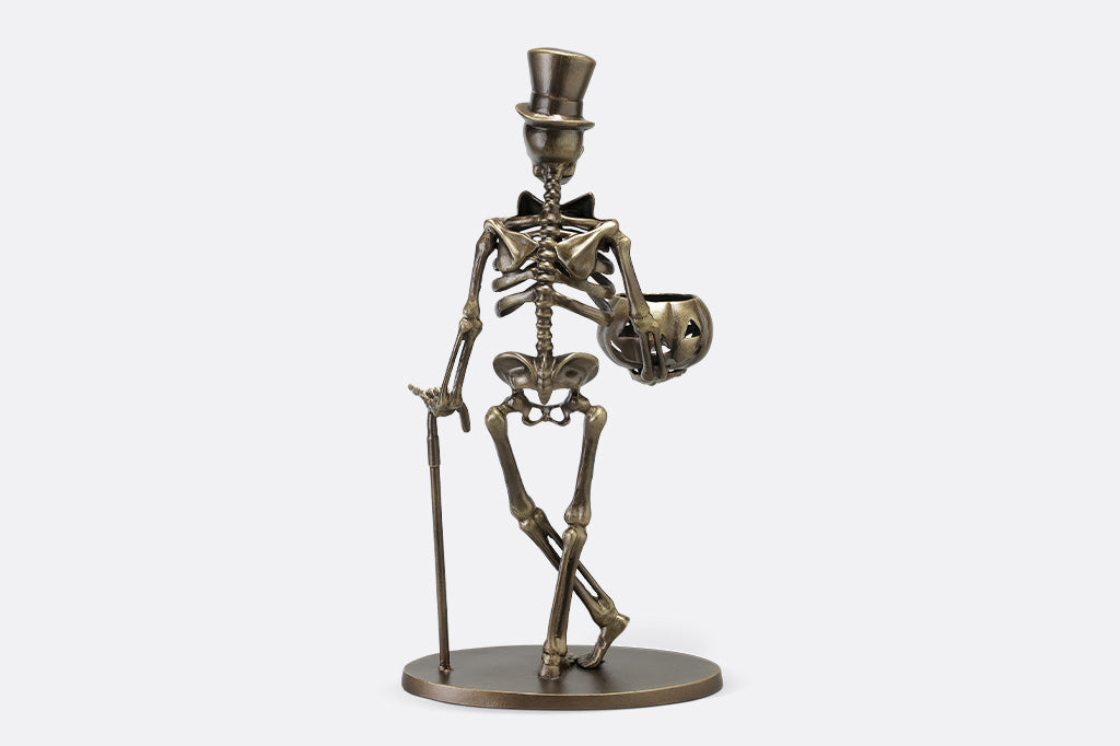 Bronze skeleton figurine with a top hat on a white background