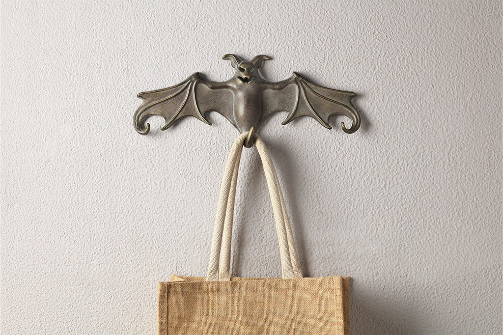 Bat-shaped wall hook with a jute bag on a plain wall