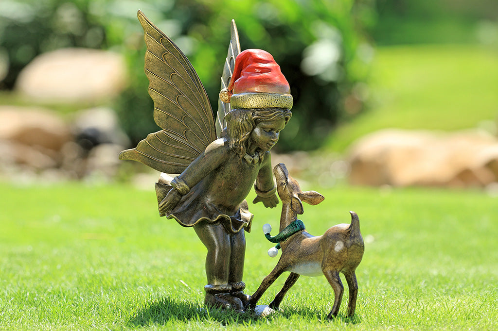 A sculpture of a fairy wearing a santa hat and a deer wearing a scarf playing with each other.