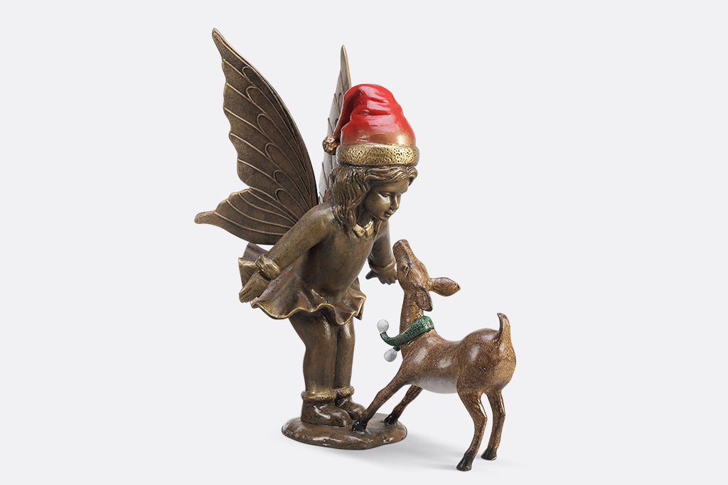 A sculpture of a fairy wearing a santa hat and a deer wearing a scarf playing with each other.