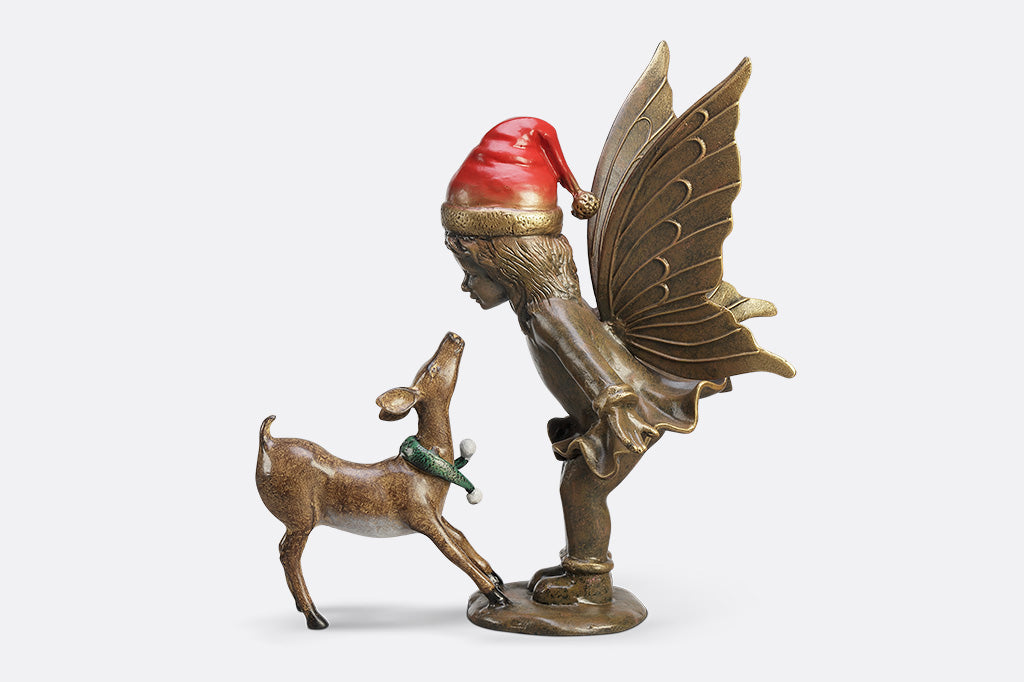 A sculpture of a fairy wearing a santa hat and a deer wearing a scarf playing with each other.