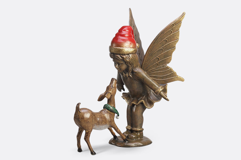 A sculpture of a fairy wearing a santa hat and a deer wearing a scarf playing with each other.