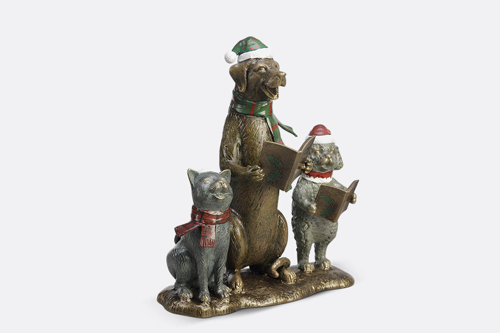 A cat and two dogs are singing and  dressed in festive christmas attire hold a book of christmas carols.