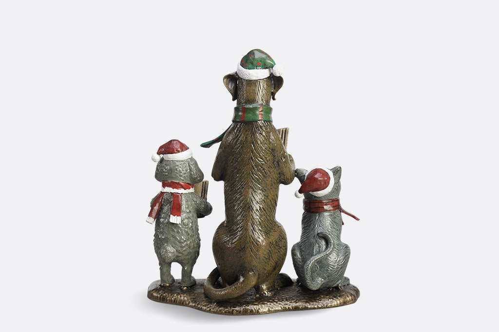 A cat and two dogs are singing and  dressed in festive christmas attire hold a book of christmas carols.