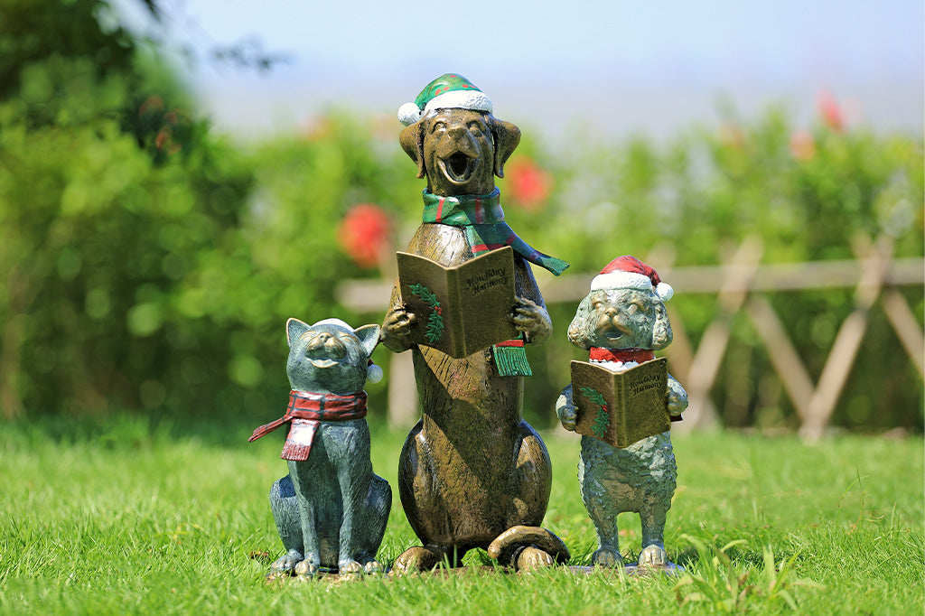 A cat and two dogs are singing and  dressed in festive christmas attire hold a book of christmas carols.