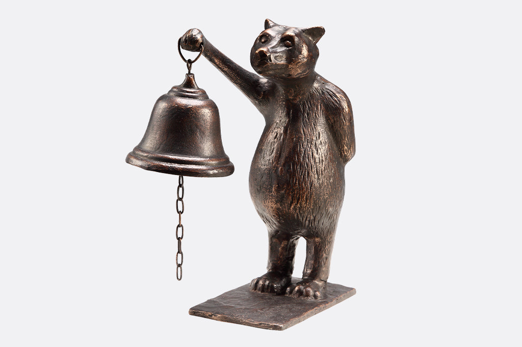 Cast iron brown bear standing on hind legs  holding bell on white background 