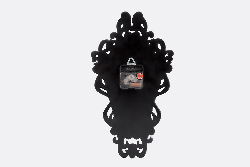 Battery slot and clock mechanism shown on backside of black decorative wall clock with intricate design on a white background