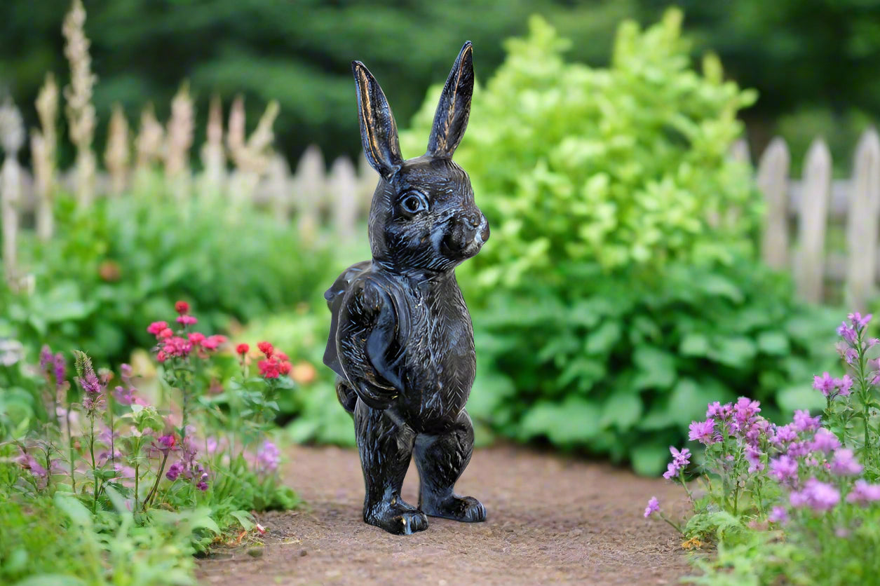 garden sculpture of bunny wearing backpack, shown on garden path near a picket fence