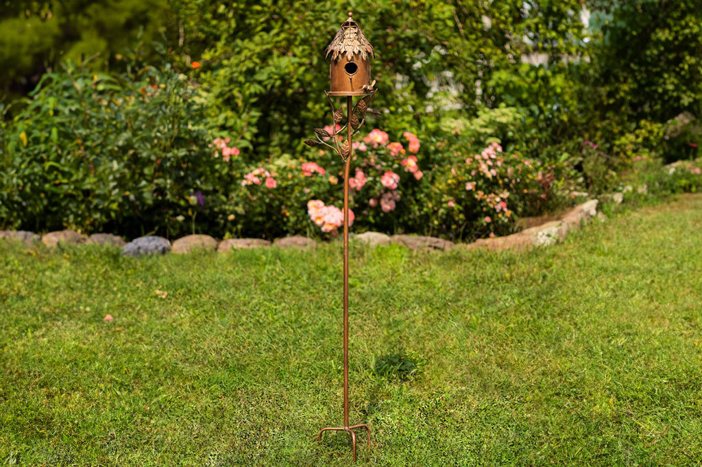 decorative metal birdhouse on a stake in a garden setting