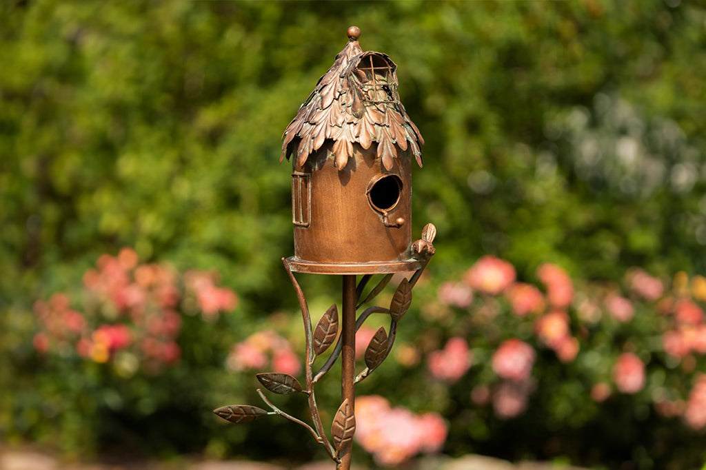 decorative metal birdhouse on a stake in a garden setting