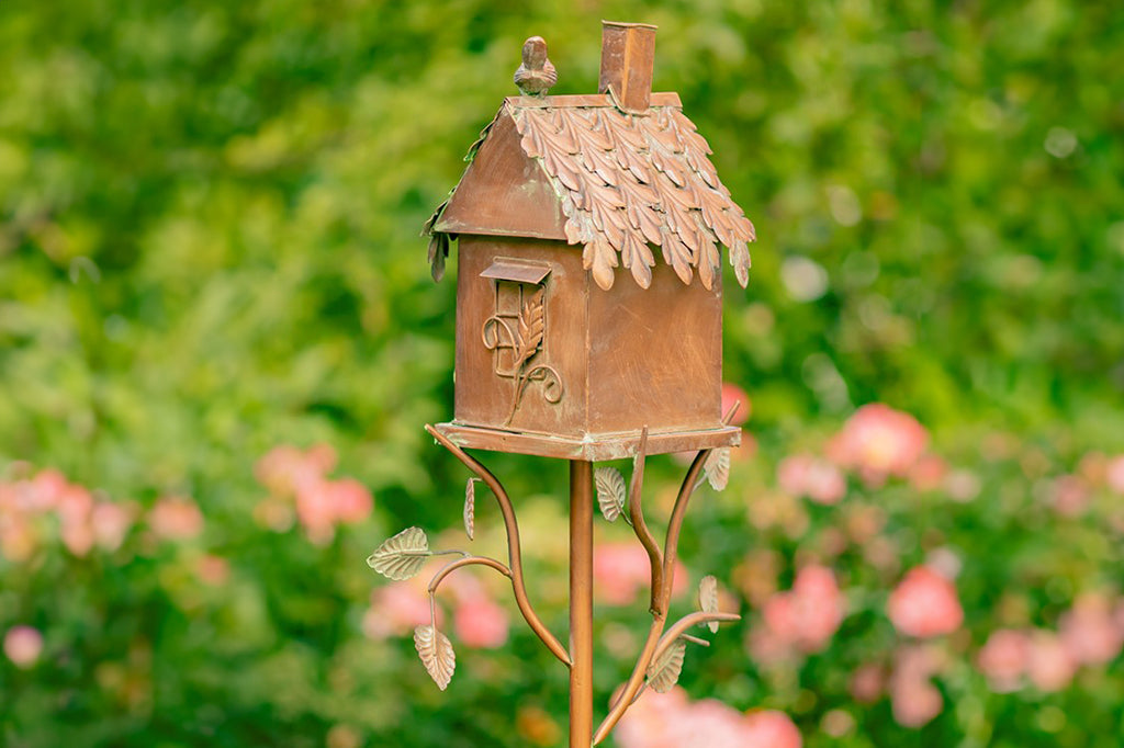 Sheet metal with copper finish forms a decorative cottage style birdhouse on a stake in garden